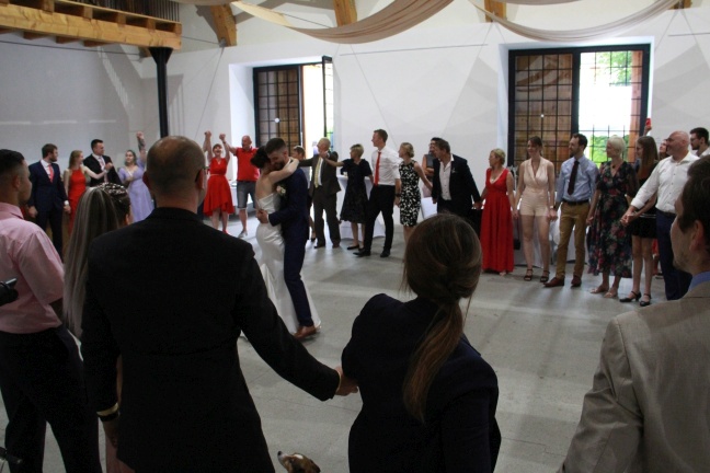 Novomanželé procházející svatebním špalírem tvořeným svatebními hosty s rukama nad hlavami