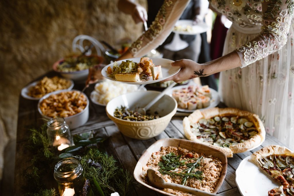 Nevěsta na svatbě nabírající si ze svatebního menu veganské jídlo umístěné na dřevěném stole