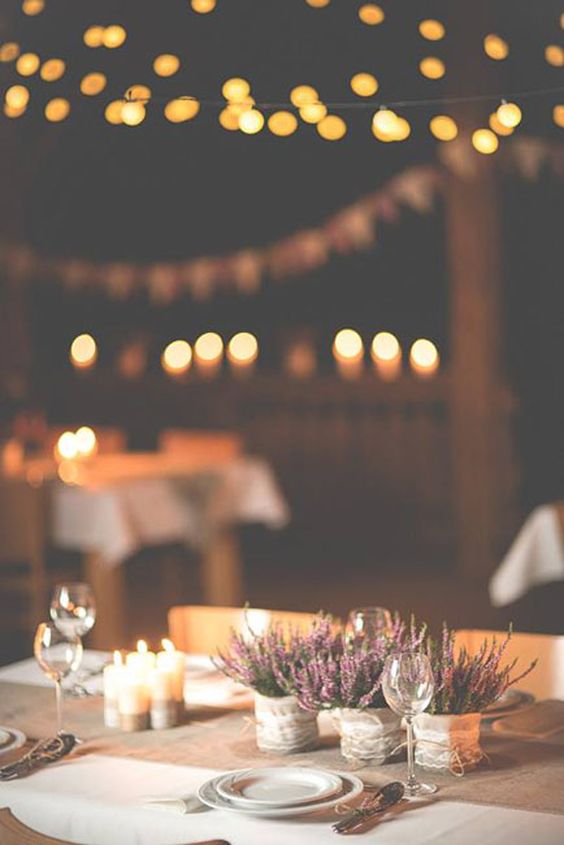 Svatební dekorace - svíčky rozmístěné uprostřed prostřené svatební tabule vedle misek s vřesem